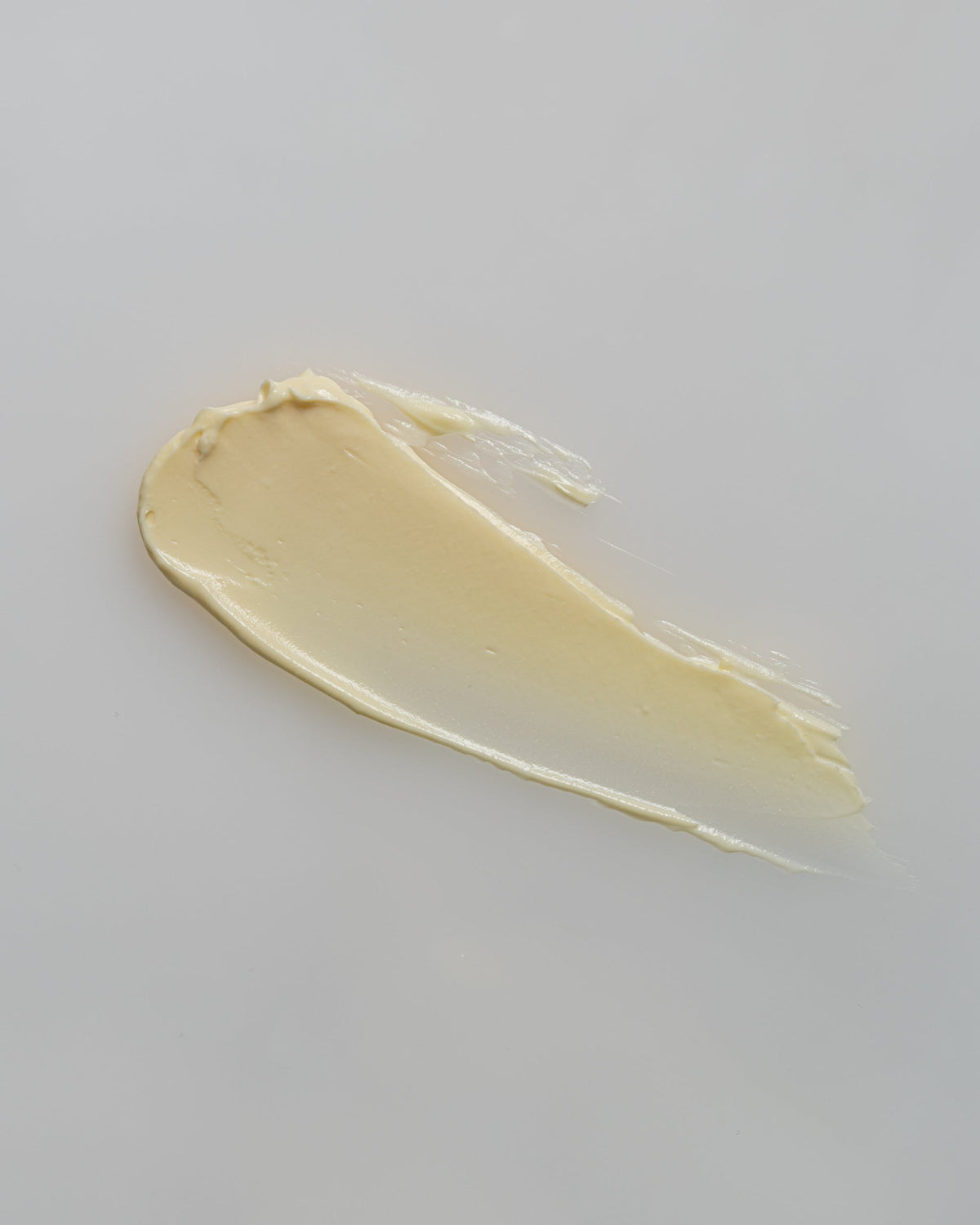 A swipe of creamy, yellow CBD Natural Relief Lotion on a white surface.