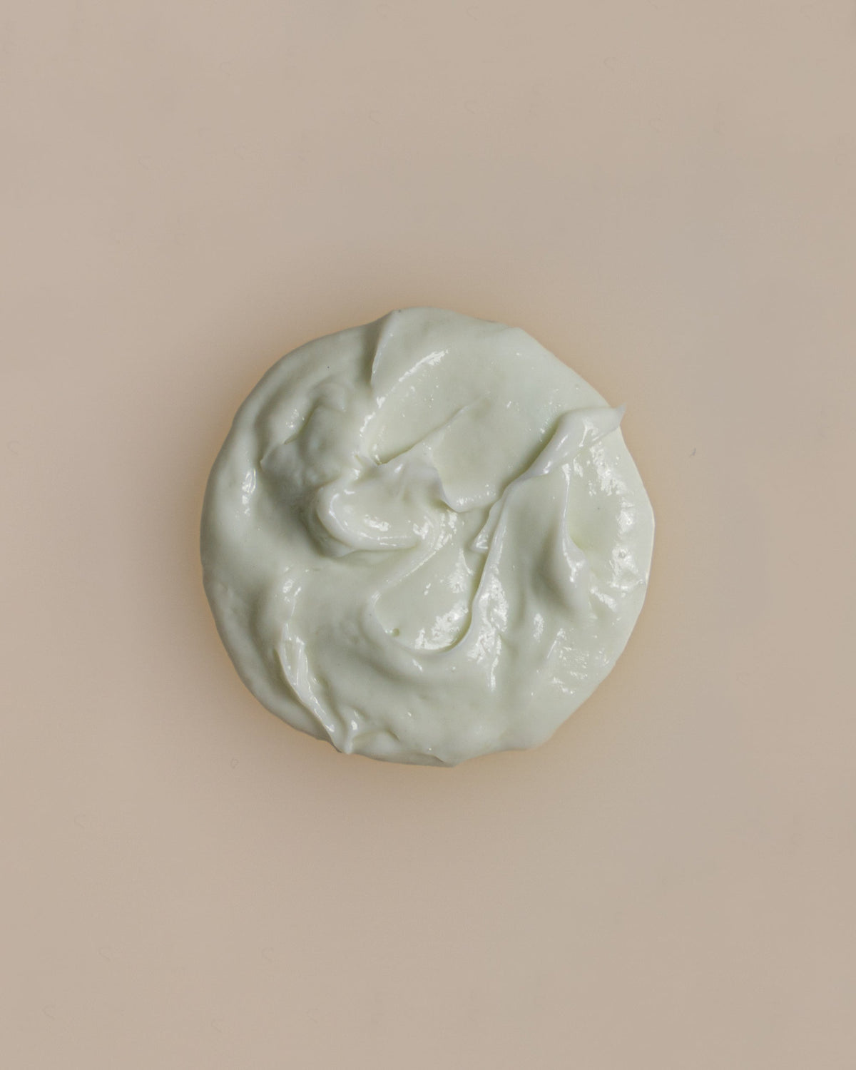 A creamy, swirly light green dollop of Dry Defense Daily Moisturizing Lotion on an off-white surface.