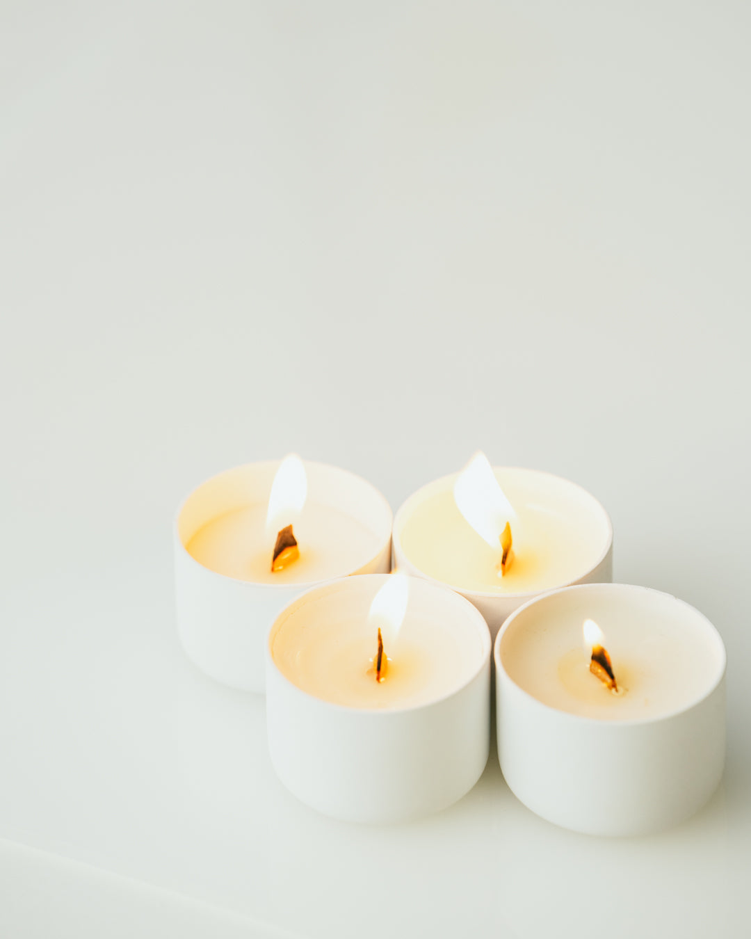 Four lit tealight candles sitting atop a white backdrop.